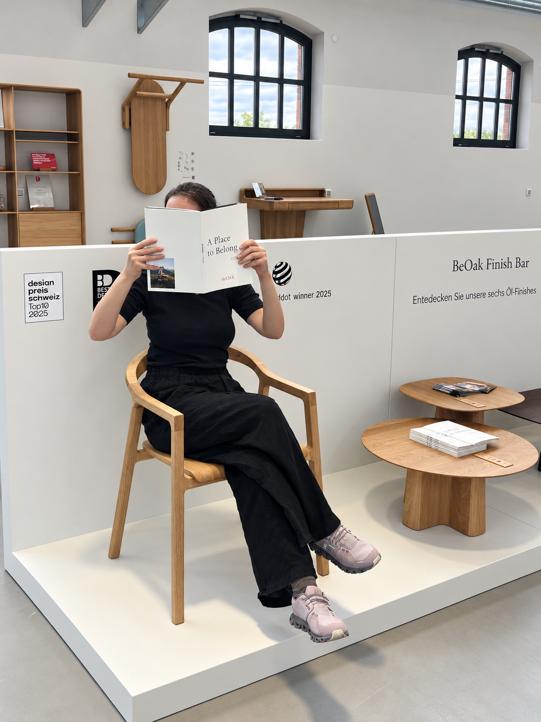 Person liest „A Place to Belong“ in einem Eichensessel am Finish Bar im Showroom Berlin